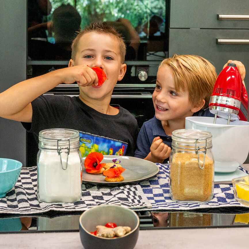 Twee jongens in de keuken met een mixer. Een jongen stopt een klaproos in zijn mond